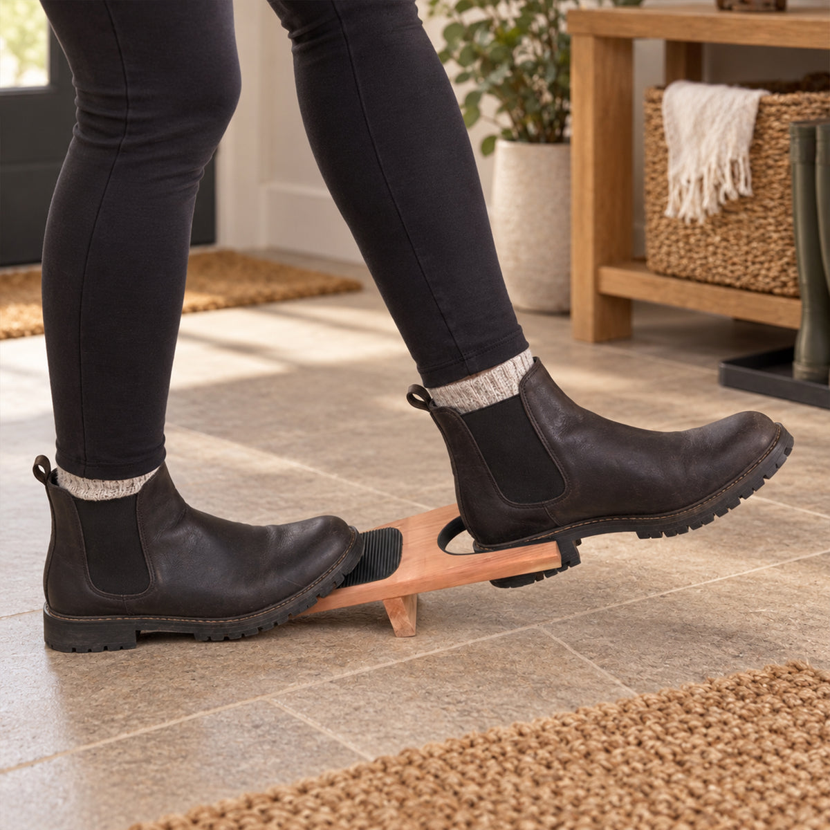 Woman using a premium cedarwood boot jack to remove ankle boots